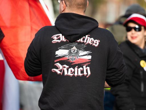 Ein Mann trägt einen Pullover mit dem Aufdruck "Deutsches Reich" bei einer Demonstration von Reichsbürgern. Sogenannte Reichsbürger und andere Demokratiegegner demonstrieren in der Nähe des Neuen Palais.