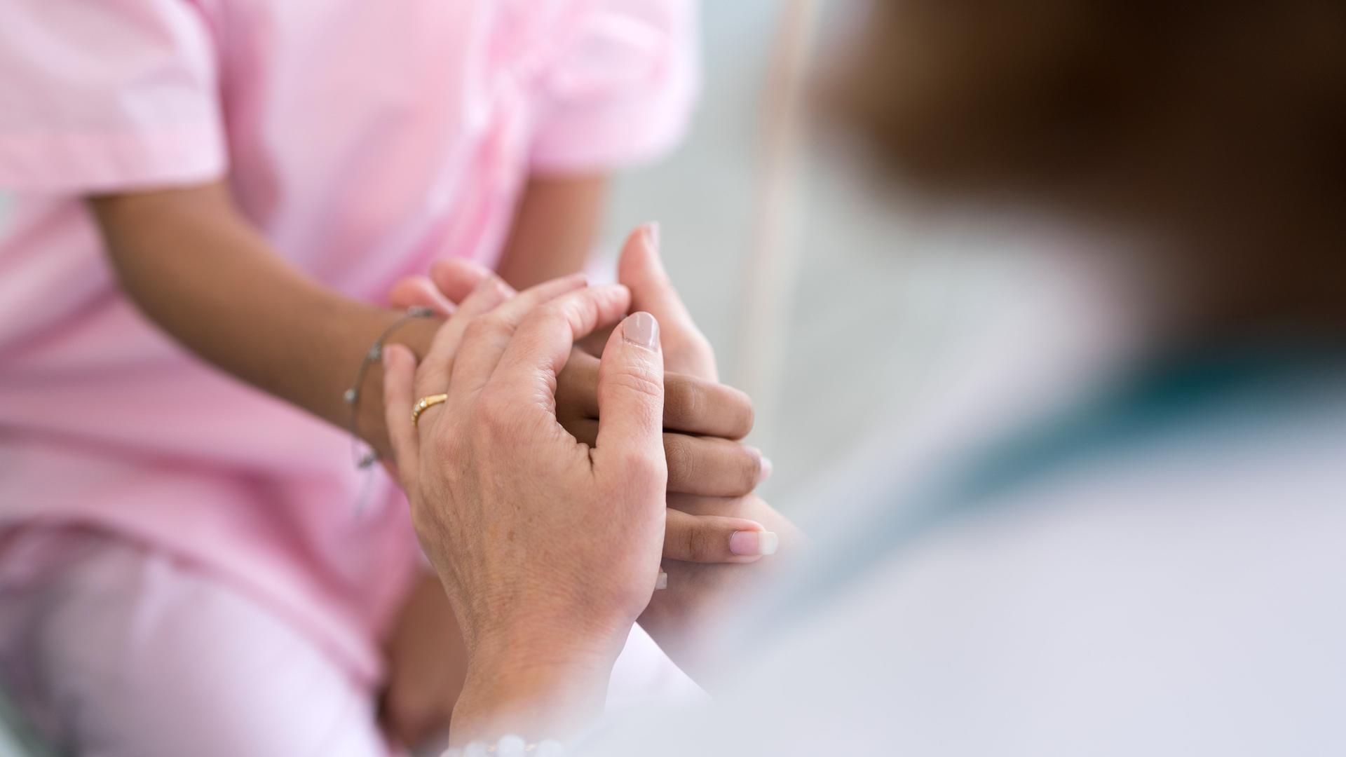 Nahaufnahme in einem Krankenhaus. Eine Person hält einer anderen Person die Hände. Nahaufnahme in einem Krankenhaus. Eine Person hält einer anderen Person die Hände.