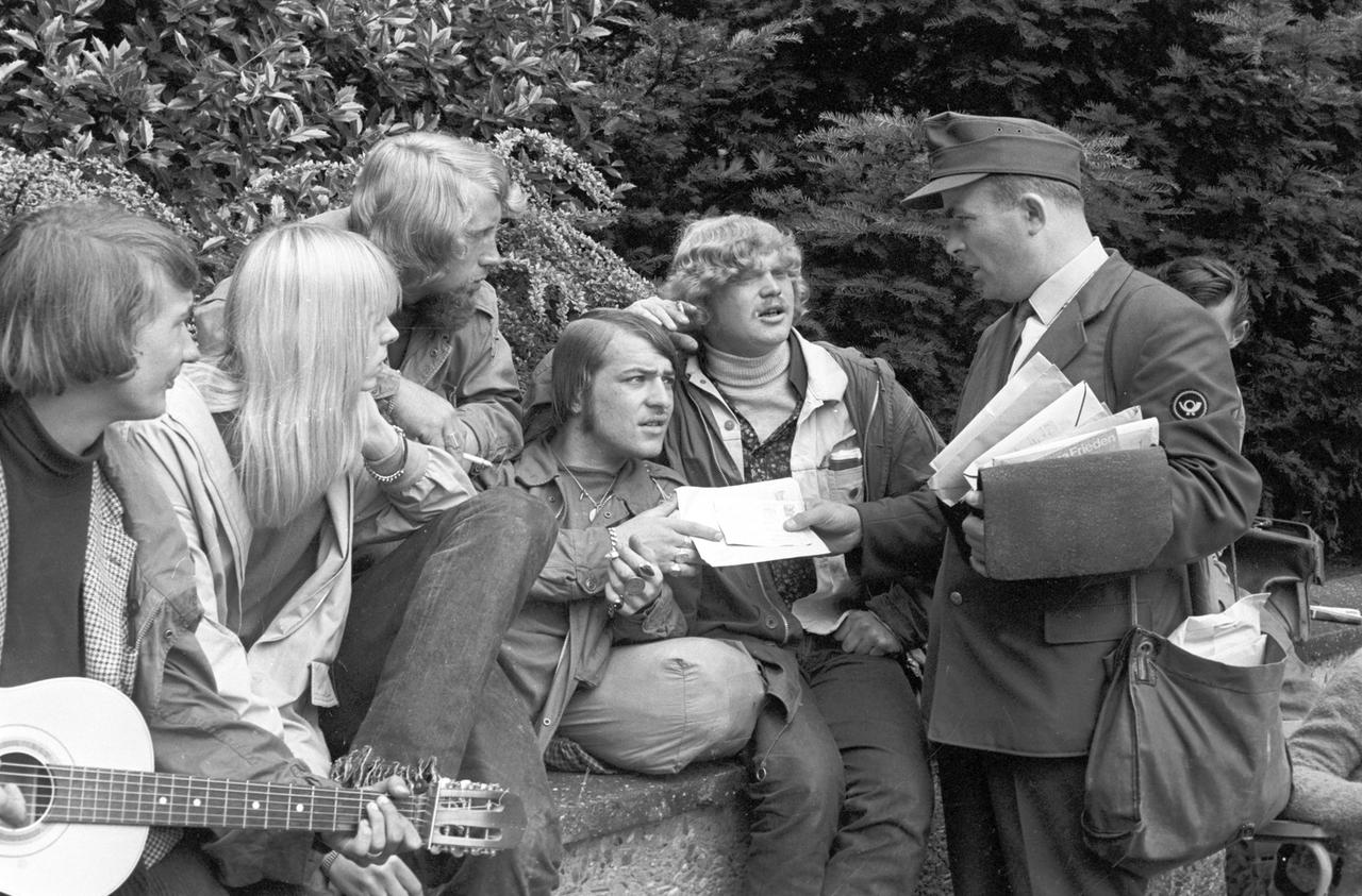 Schwarz-weiß-Foto von 1967: Eine Gruppe von jungen Hippies im Park bekommt von einem Briefträger Post zugesteckt.