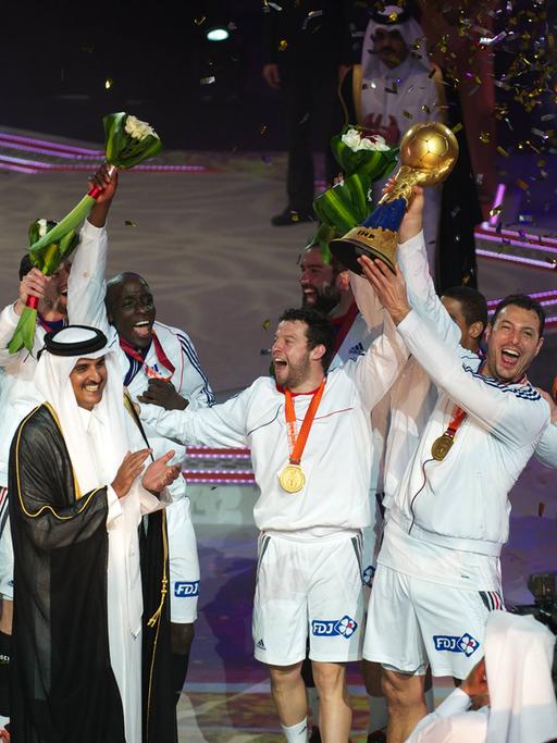 Französische Handballspieler jubeln bei der Siegerehrung der Handball-Weltmeisterschaft 2015 in Katar. Vor ihnen stehen Scheich Tamim bin Hamad Al Thani und Weltverbandspräsident Hassan Moustafa und klatschen in die Hände. 