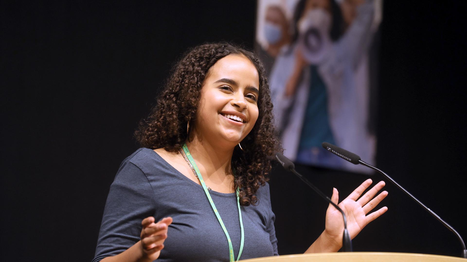 Sarah-Lee Heinrich, die Co-Bundessprecherin der Grünen Jugend, spricht beim 55. Bundeskongress der Parteijugend. Sie steht an einem Pult und blickt lächelnd ins Pubikum.