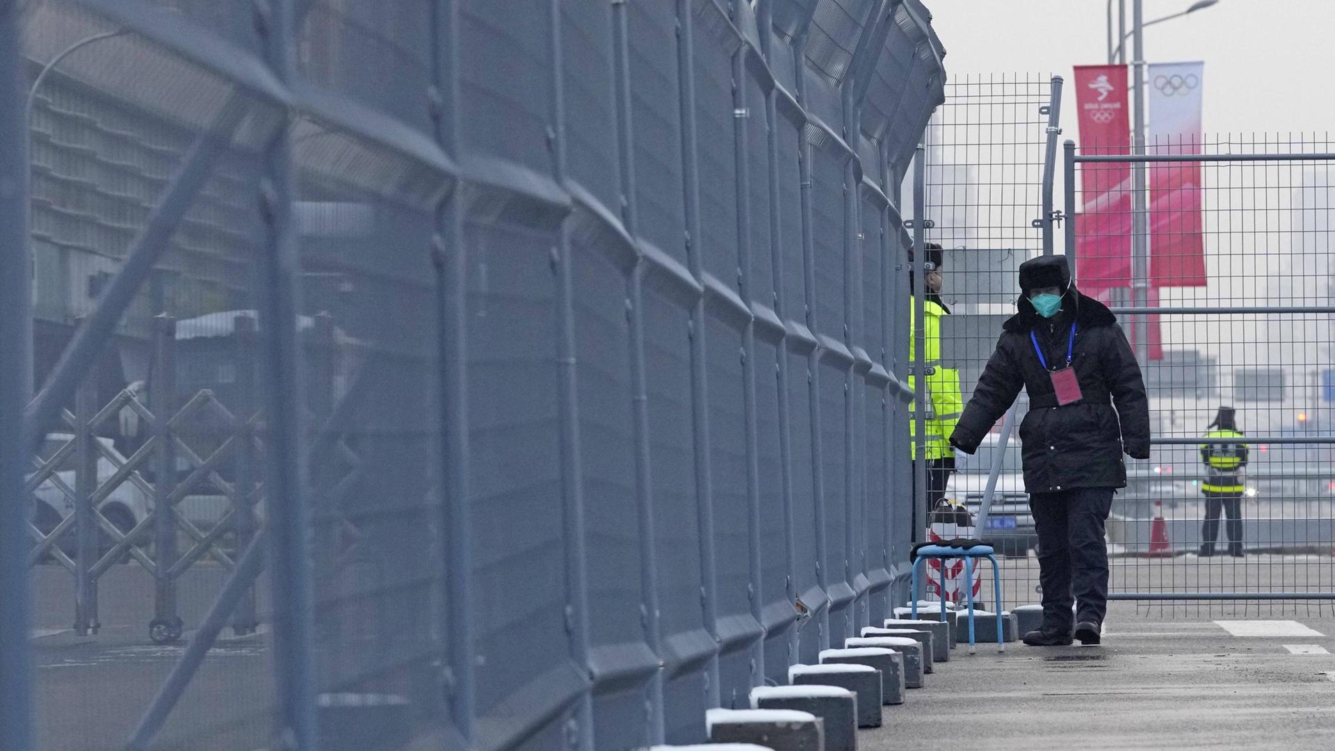 Wachpersonal mit Maske geht am 22. Januar einen Zaun vor einer Olympiastätte in Peking entlang. Wachpersonal mit Maske geht am 22. Januar einen Zaun vor einer Olympiastätte in Peking entlang.