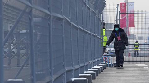 Wachpersonal mit Maske geht am 22. Januar einen Zaun vor einer Olympiastätte in Peking entlang. 