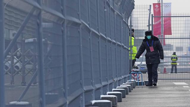 Wachpersonal mit Maske geht am 22. Januar einen Zaun vor einer Olympiastätte in Peking entlang. 