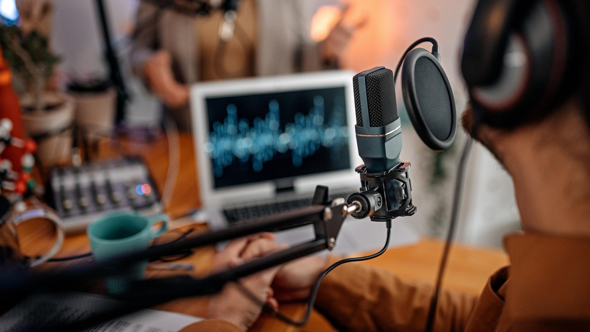 Zwei Personen sitzen in einem Studio vor Mikrofonen und Laptops. Zwei Personen sitzen in einem Studio vor Mikrofonen und Laptops.