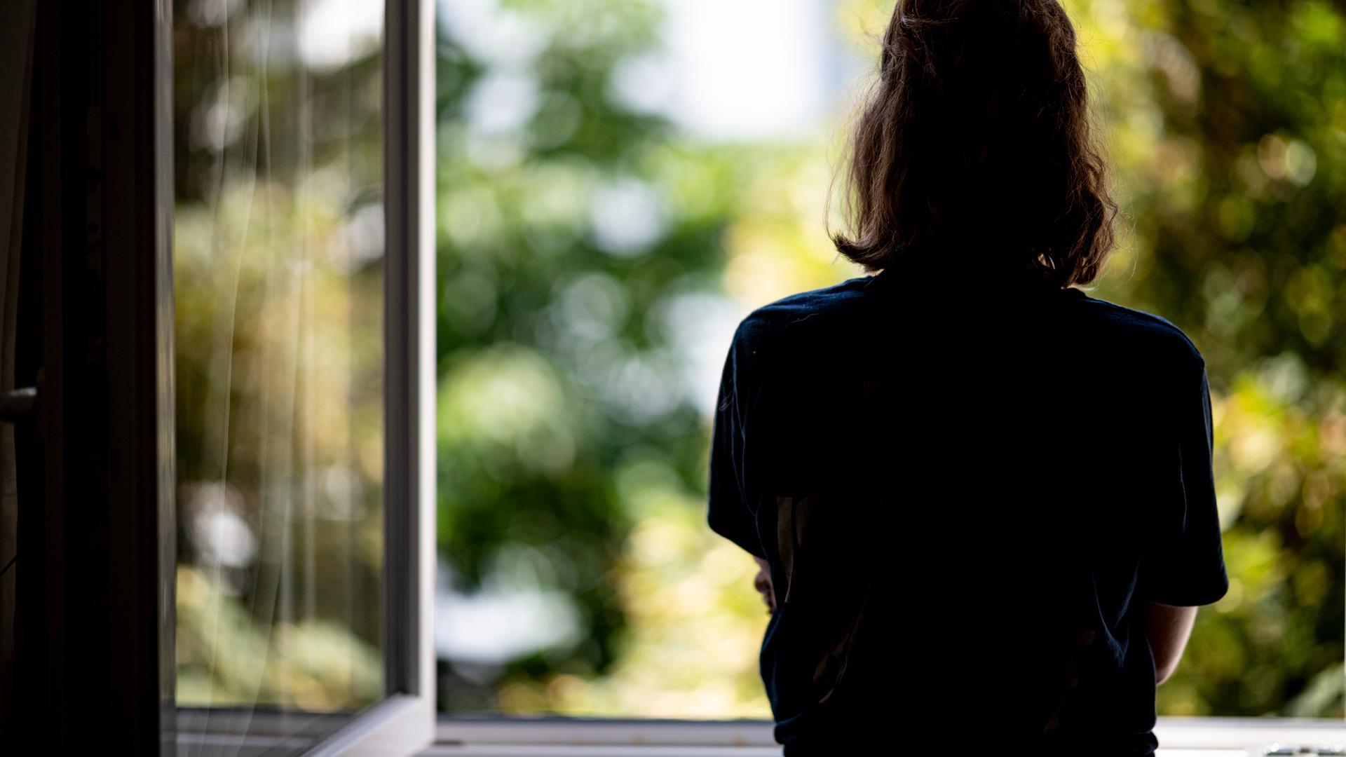 Eine Frau steht in ihrer Wohnung an einem Fenster. 