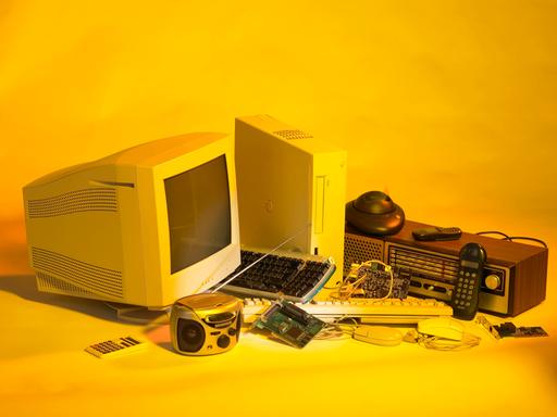 Elektroschrott wie ein alter PC und alte Handys vor gelben Hintergrund.