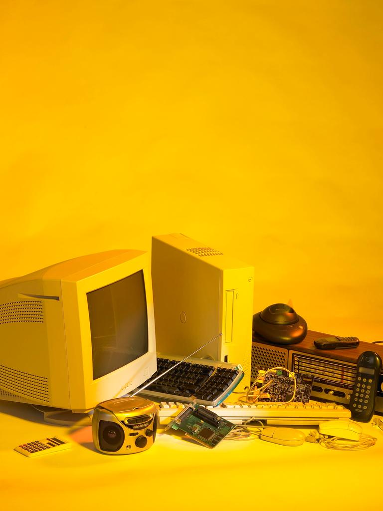 Elektroschrott wie ein alter PC und alte Handys vor gelben Hintergrund.