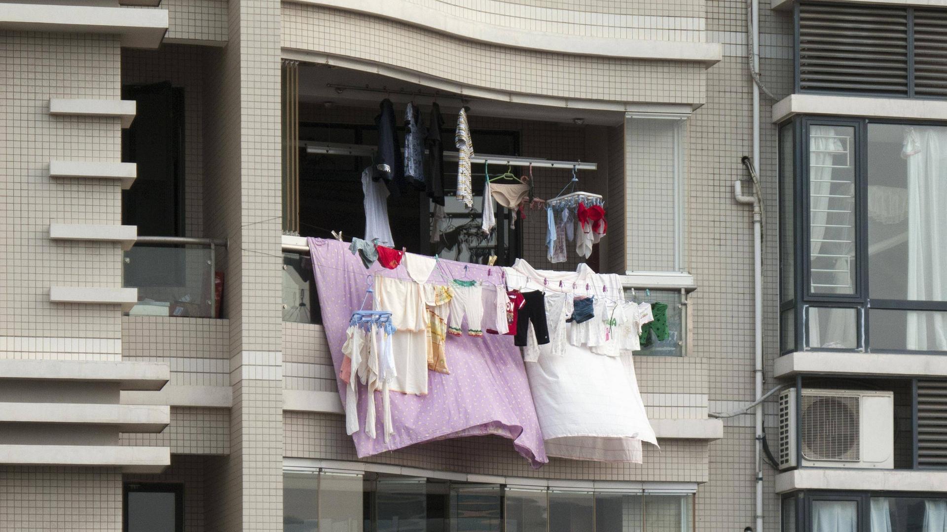 Bunte Wäsche hängt von einem Balkon eines Hochhauses.