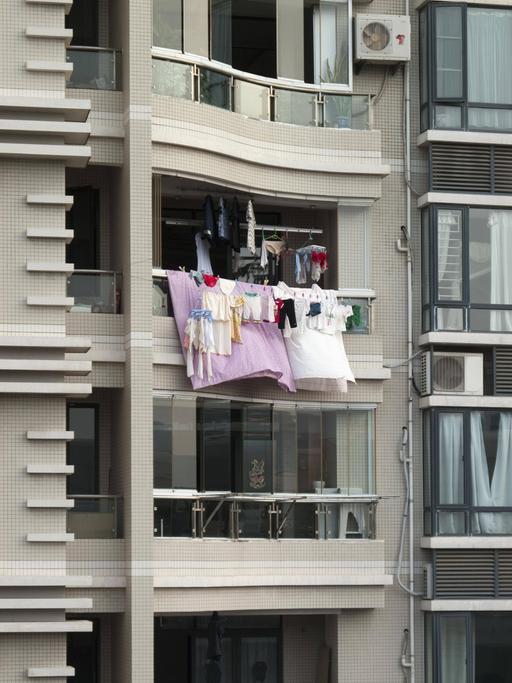 Bunte Wäsche hängt von einem Balkon eines Hochhauses.