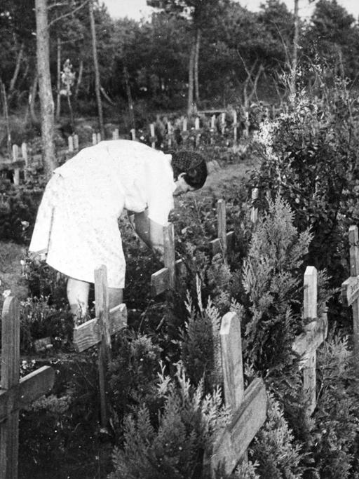 Altes Schwarz-Weiß-Foto einer Frau, die sich auf dem Friedhof von Oksbøl über ein Grab beugt.