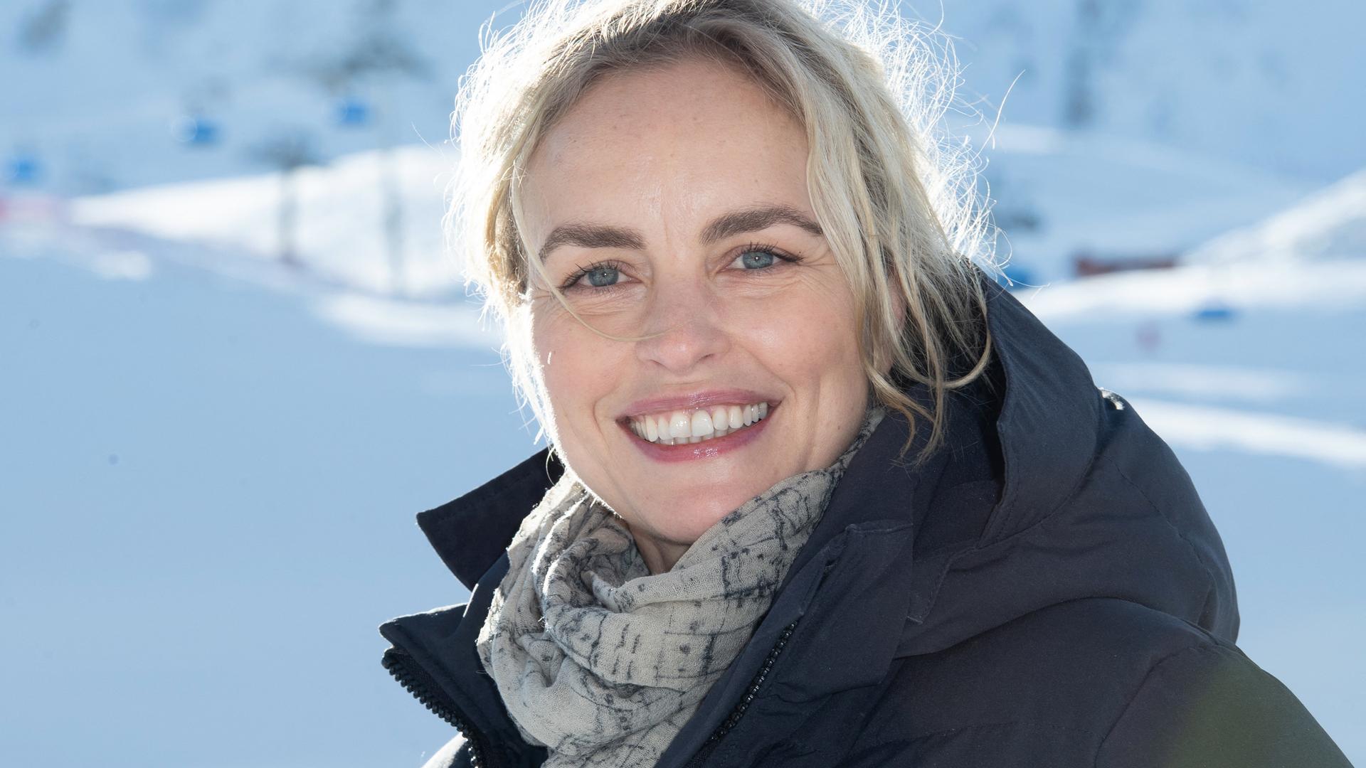 Nina Hoss steht freundlich lachend in einer Schneelandschaft