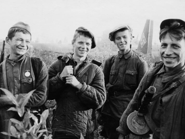 Vier junge Partisanen grinsen vor einem Flugzeug der Nazis in die Kamera