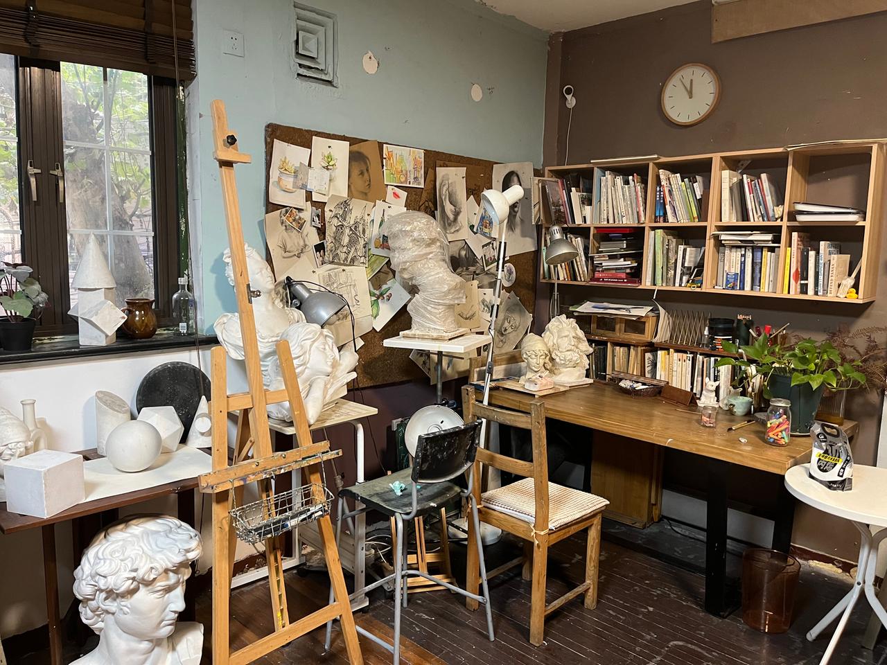 Ein Atelier mit Staffelei, Skulpturen und vielen Büchern im Regal. Ein Atelier mit Staffelei, Skulpturen und vielen Büchern im Regal.