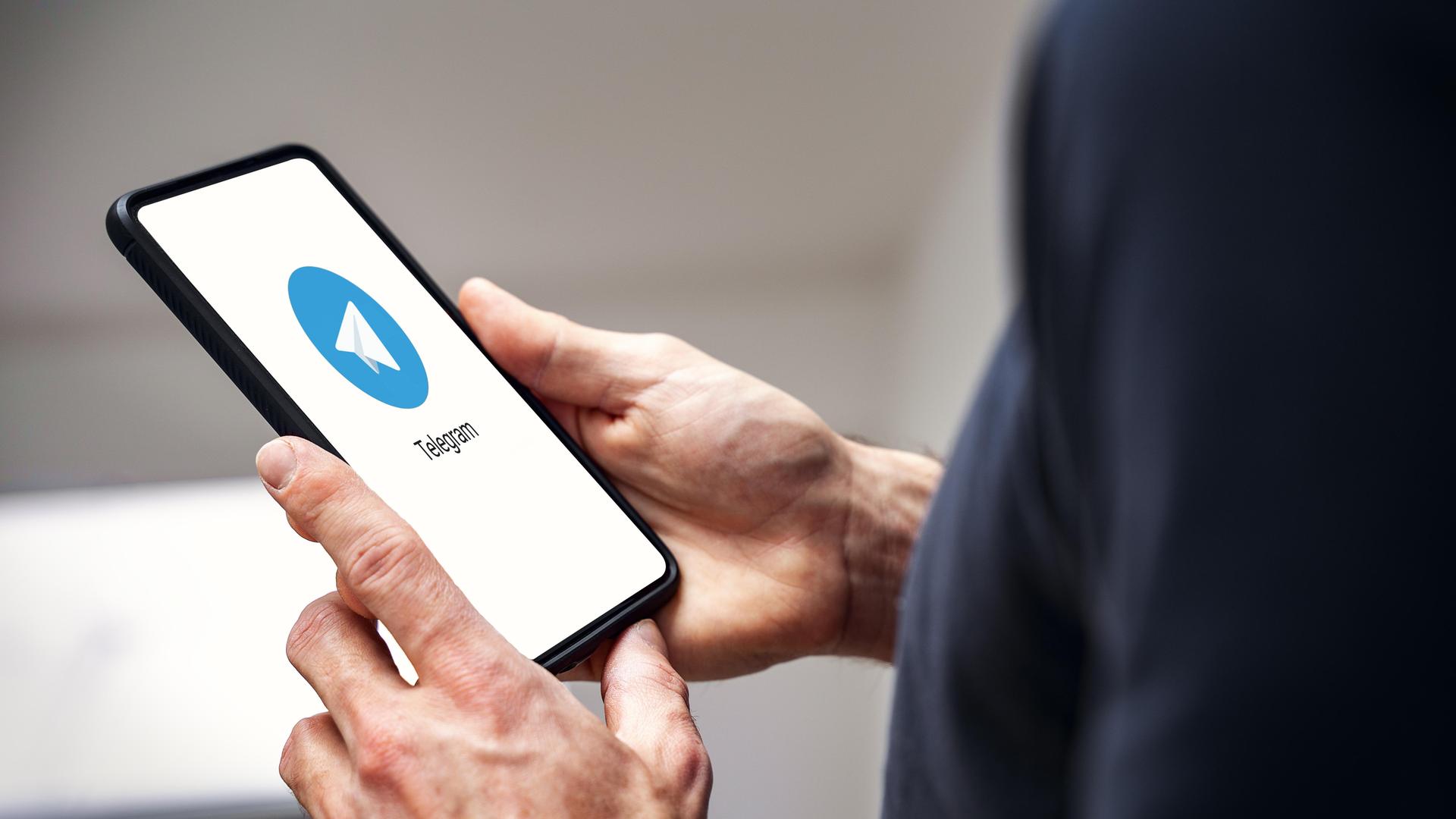 Die Hand eines Mannes mit einem Smartphone mit Telegram Messenger App auf dem Bildschirm (Fotomontage). Die Hand eines Mannes mit einem Smartphone mit Telegram Messenger App auf dem Bildschirm (Fotomontage).
