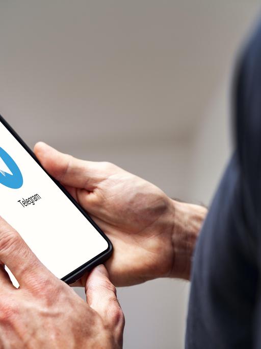 Die Hand eines Mannes mit einem Smartphone mit Telegram Messenger App auf dem Bildschirm (Fotomontage).