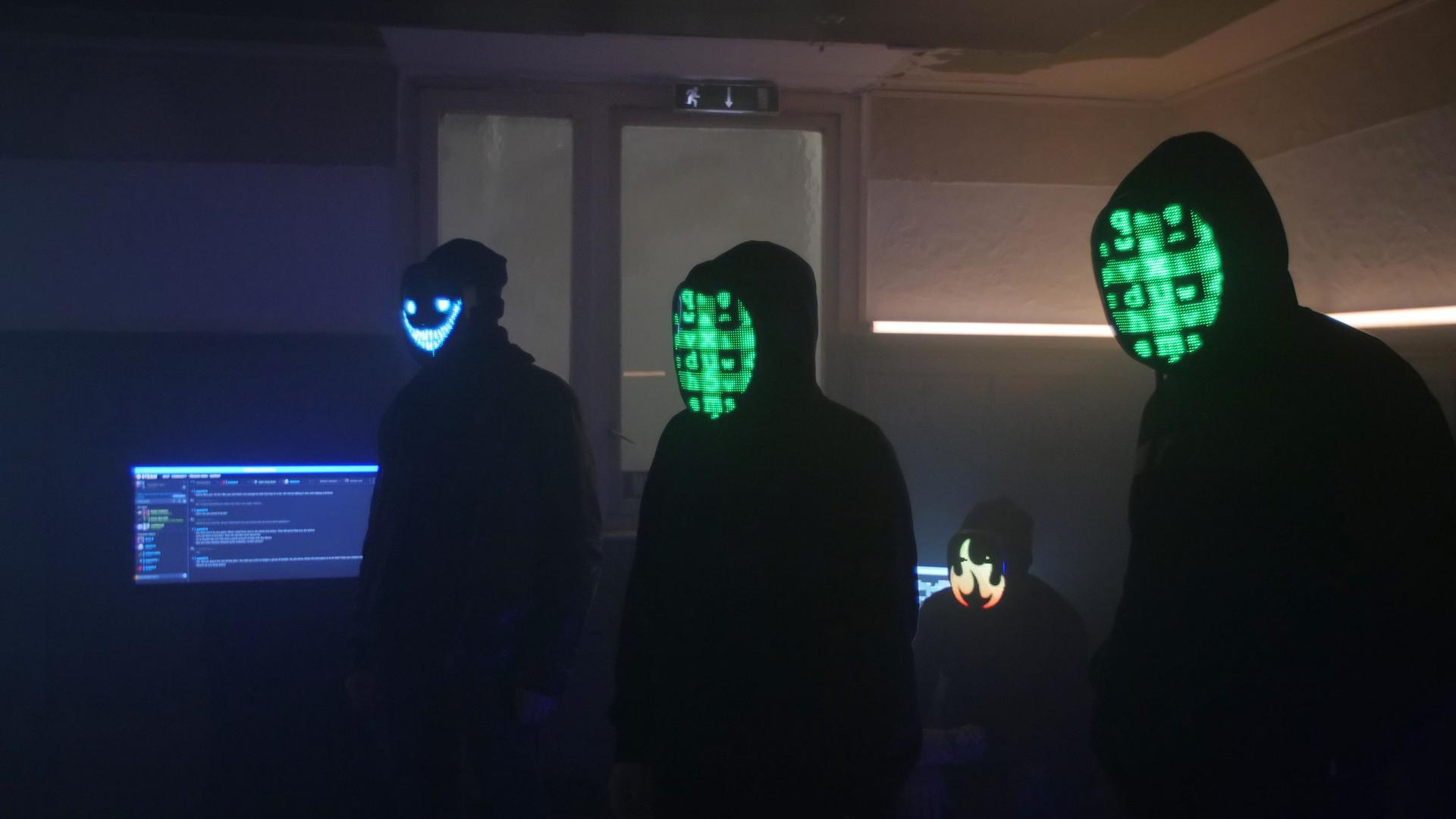 Schwarze Silhouetten von vermeintlich jungen Männern mit Kapuzenpullis in einem abgedunkelten Raum. Ihre Gesichter sind mit digitalen Codes unkenntlich gemacht. Schwarze Silhouetten von vermeintlich jungen Männern mit Kapuzenpullis in einem abgedunkelten Raum. Ihre Gesichter sind mit digitalen Codes unkenntlich gemacht.