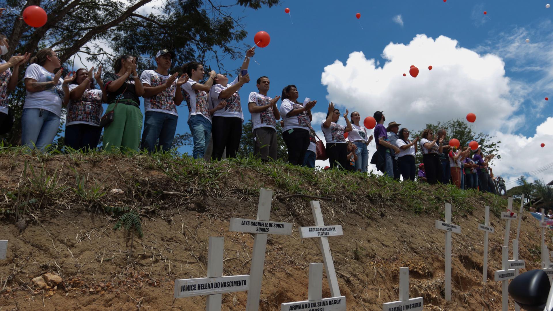 Angehörige der Opfer lassen Luftballons steigen. Im Vordergrund sind weiße Holzkreuze mit den Namen der Toten.