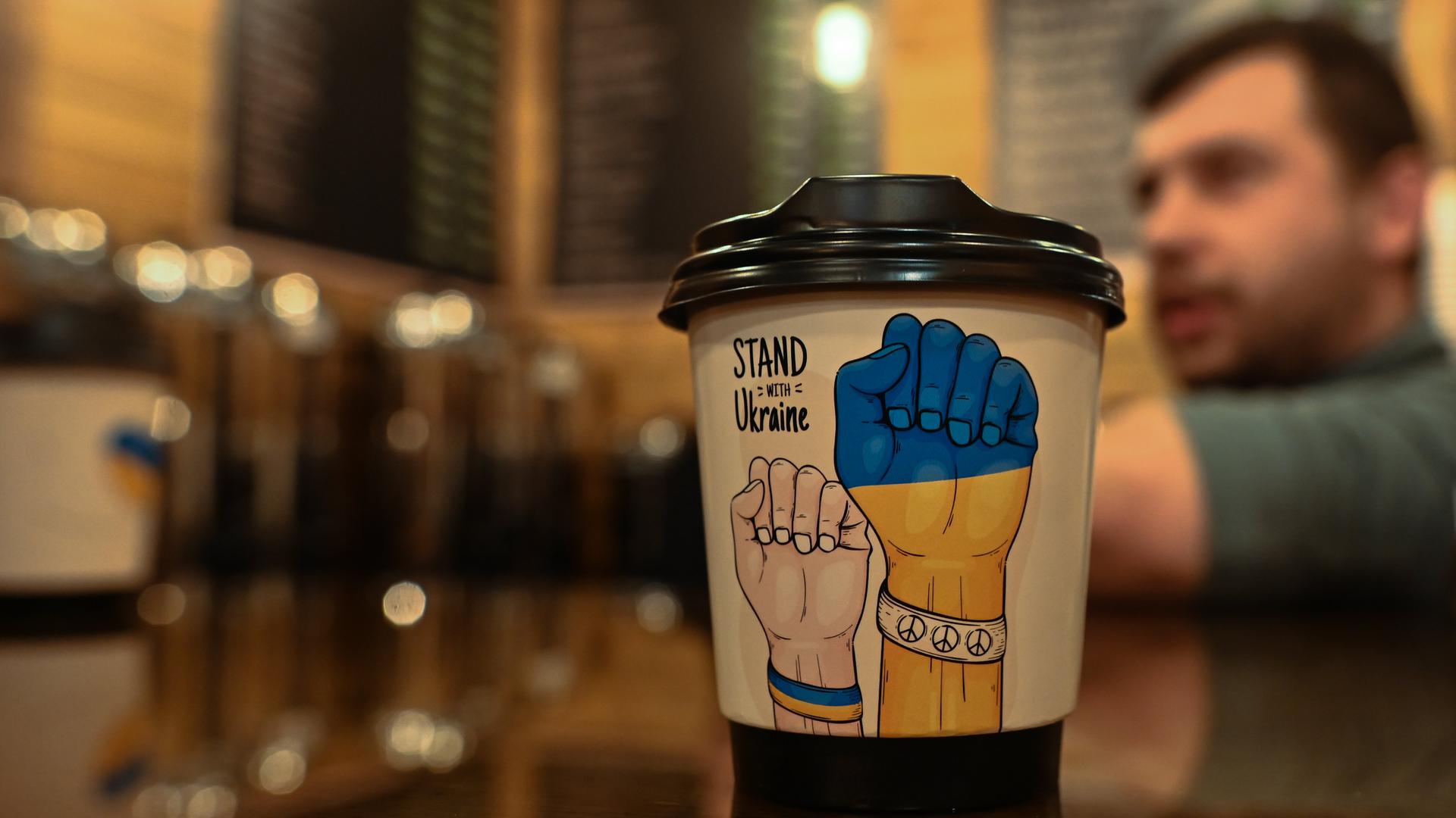 Ein Kaffeebecher mit symbolischen Bildern und der Aufschrift "Stand with Ukraine" in einem Cafe in der westukrainischen Stadt Chmelnyzkyj