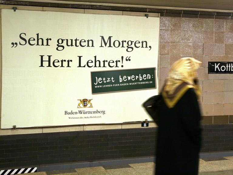 Eine Frau läuft in einem Berliner U-Bahnhof an einem Werbeplakat vorbei, auf dem Baden-Württemberg für den Lehrerberuf wirbt. Darauf steht in einer altmodischen Schrift der Satz: "Sehr guten Morgen, Herr Lehrer." 