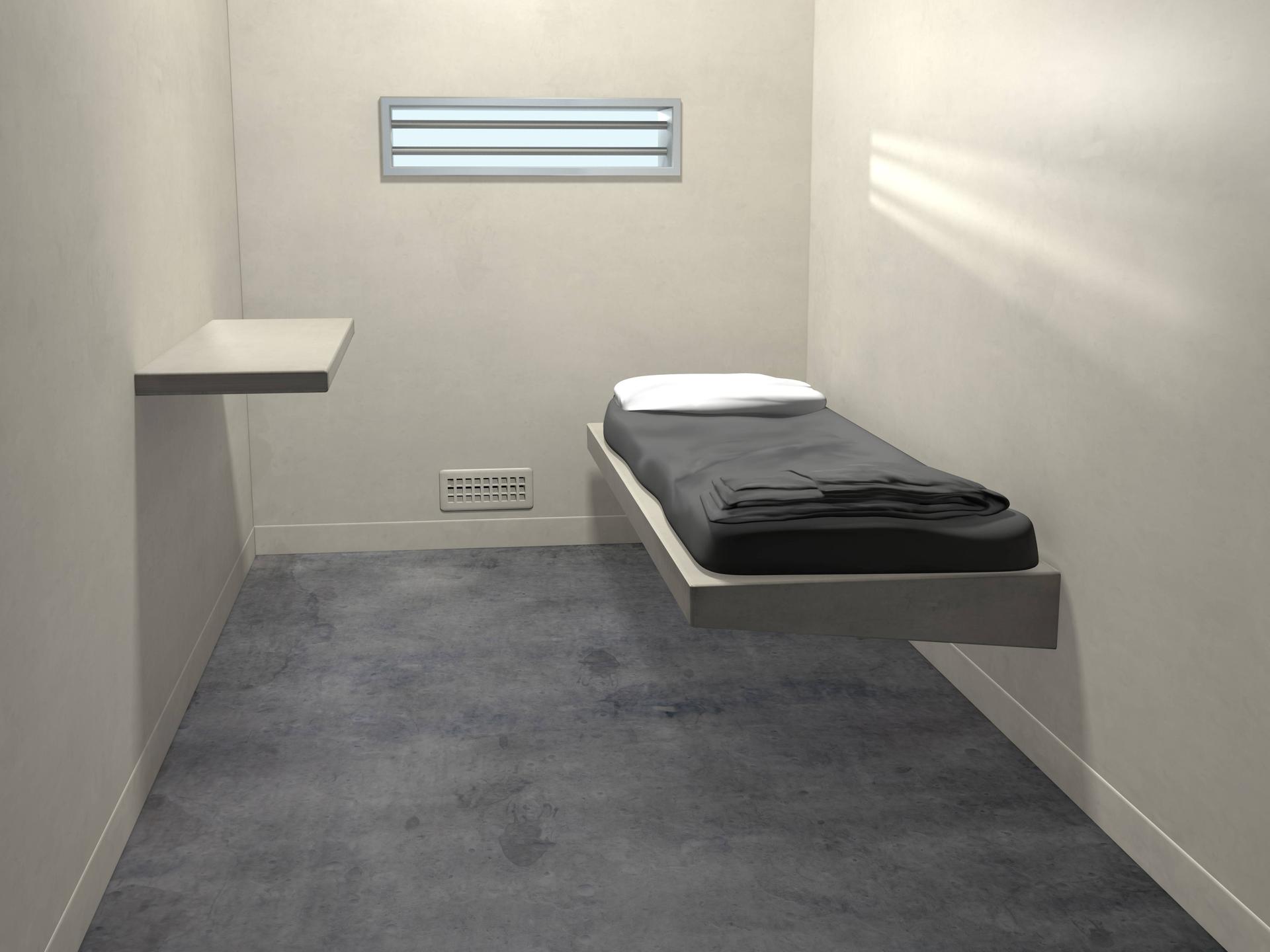 In einer Gefängniszelle steht ein Bett. 