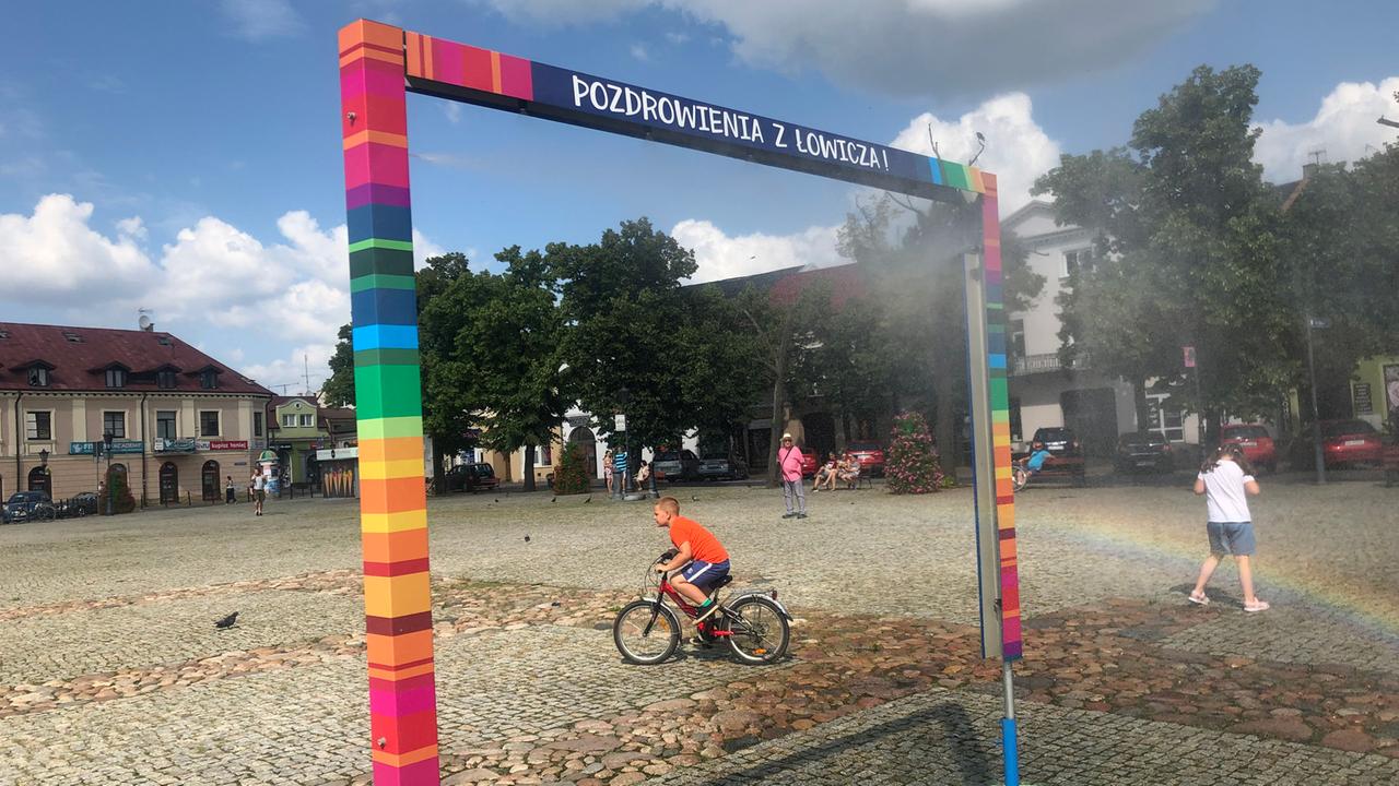 Es ist nicht, wie es scheint. Die bunten Farben auf dem Marktplatz von Łowicz nördöstlich von Łódź verweisen auf traditionelle Volkskunst – nicht auf die LGBT-Flagge. Zu sehen: Ein Spielplatz in Lowicz, Polen. Ein Kind auf einem Fahrrad durchquert das Bild. Es ist nicht, wie es scheint. Die bunten Farben auf dem Marktplatz von Łowicz nördöstlich von Łódź verweisen auf traditionelle Volkskunst – nicht auf die LGBT-Flagge. Zu sehen: Ein Spielplatz in Lowicz, Polen. Ein Kind auf einem Fahrrad durchquert das Bild.