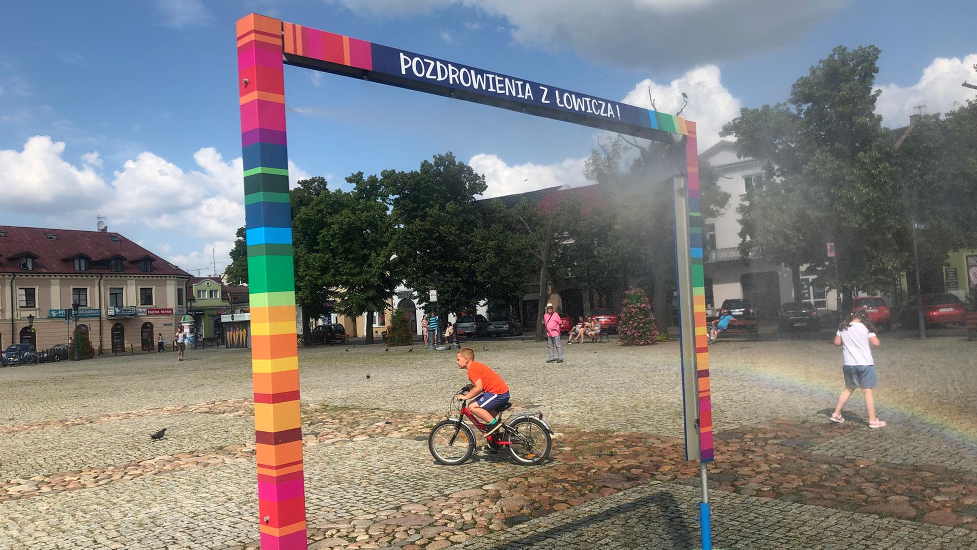 Es ist nicht, wie es scheint. Die bunten Farben auf dem Marktplatz von Łowicz nördöstlich von Łódź verweisen auf traditionelle Volkskunst – nicht auf die LGBT-Flagge. Zu sehen: Ein Spielplatz in Lowicz, Polen. Ein Kind auf einem Fahrrad durchquert das Bild. Es ist nicht, wie es scheint. Die bunten Farben auf dem Marktplatz von Łowicz nördöstlich von Łódź verweisen auf traditionelle Volkskunst – nicht auf die LGBT-Flagge. Zu sehen: Ein Spielplatz in Lowicz, Polen. Ein Kind auf einem Fahrrad durchquert das Bild.