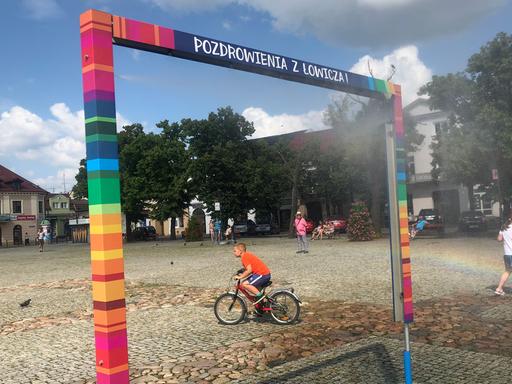 Es ist nicht, wie es scheint. Die bunten Farben auf dem Marktplatz von Łowicz nördöstlich von Łódź verweisen auf traditionelle Volkskunst – nicht auf die LGBT-Flagge. Zu sehen: Ein Spielplatz in Lowicz, Polen. Ein Kind auf einem Fahrrad durchquert das Bild. 