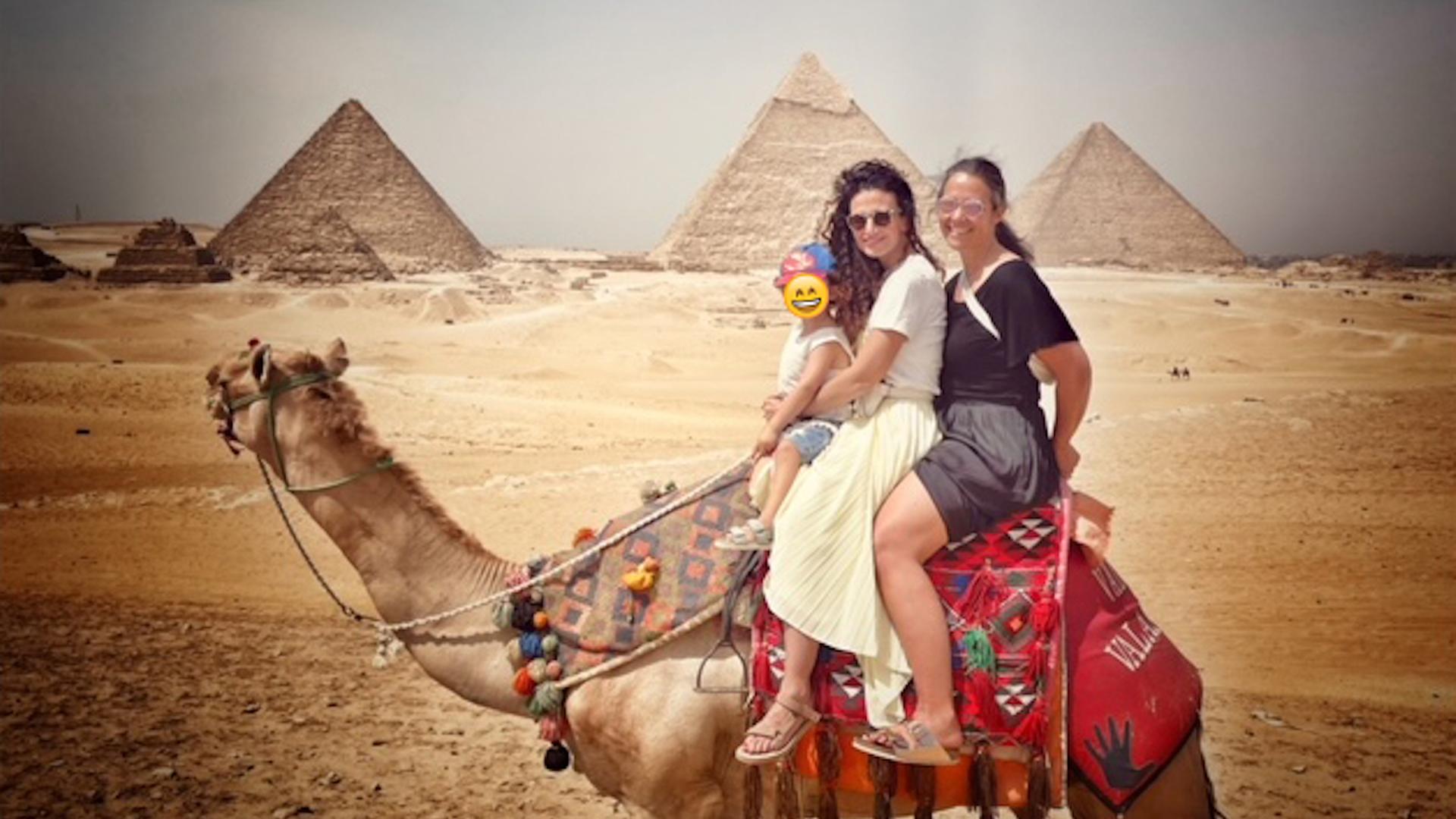 Sonja Koppitz und Marwa Eldessouky sitzen auf einem Dromedar, im Hintergrund sind die Pyramiden zu sehen.