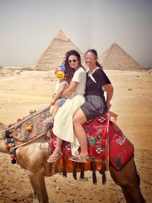Sonja Koppitz und Marwa Eldessouky sitzen auf einem Dromedar, im Hintergrund sind die Pyramiden zu sehen.