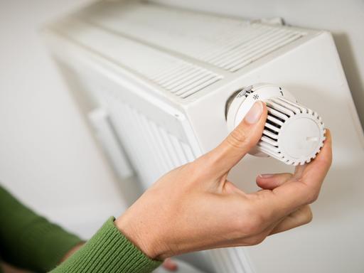 Eine Hand dreht am Temperaturregler einer Heizung. 