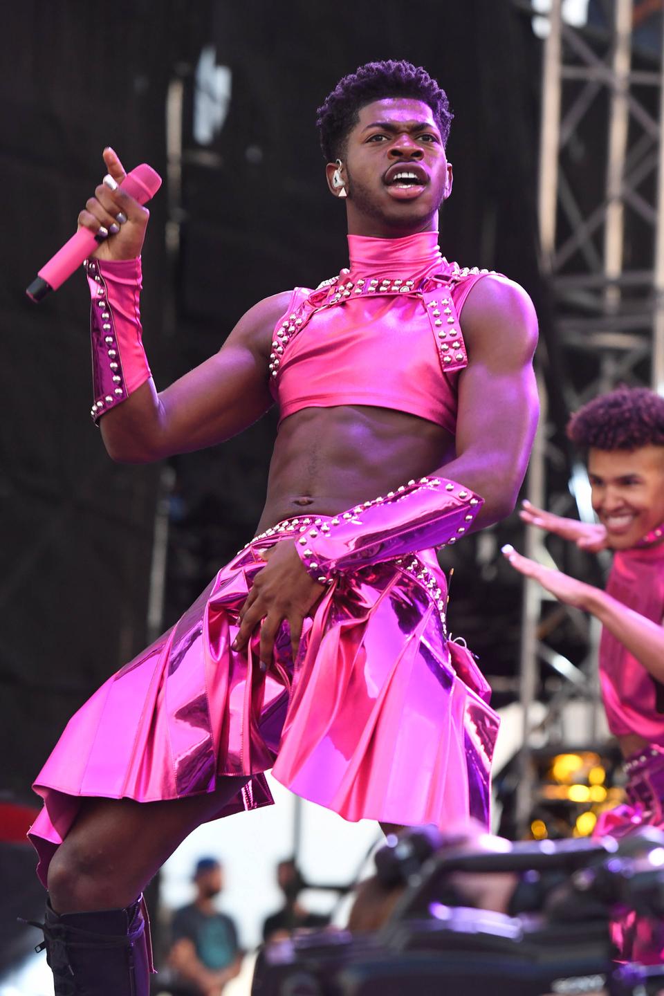 Der schwarze Rapper Lil Nas X steht auf der Bühne in einem pinken Röckchen, pinken Top und hält ein pinkes Mikrofon in der Hand. Mit der anderen Hand fast er sich in den Schritt.