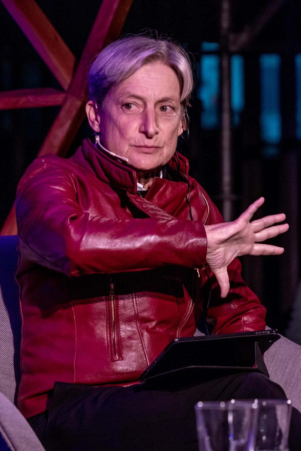 Porträtaufnahme der Philosophin Judith Butler in roter Lederjacke während einer Diskussionsveranstaltung auf einer Bühne. Porträtaufnahme der Philosophin Judith Butler in roter Lederjacke während einer Diskussionsveranstaltung auf einer Bühne.