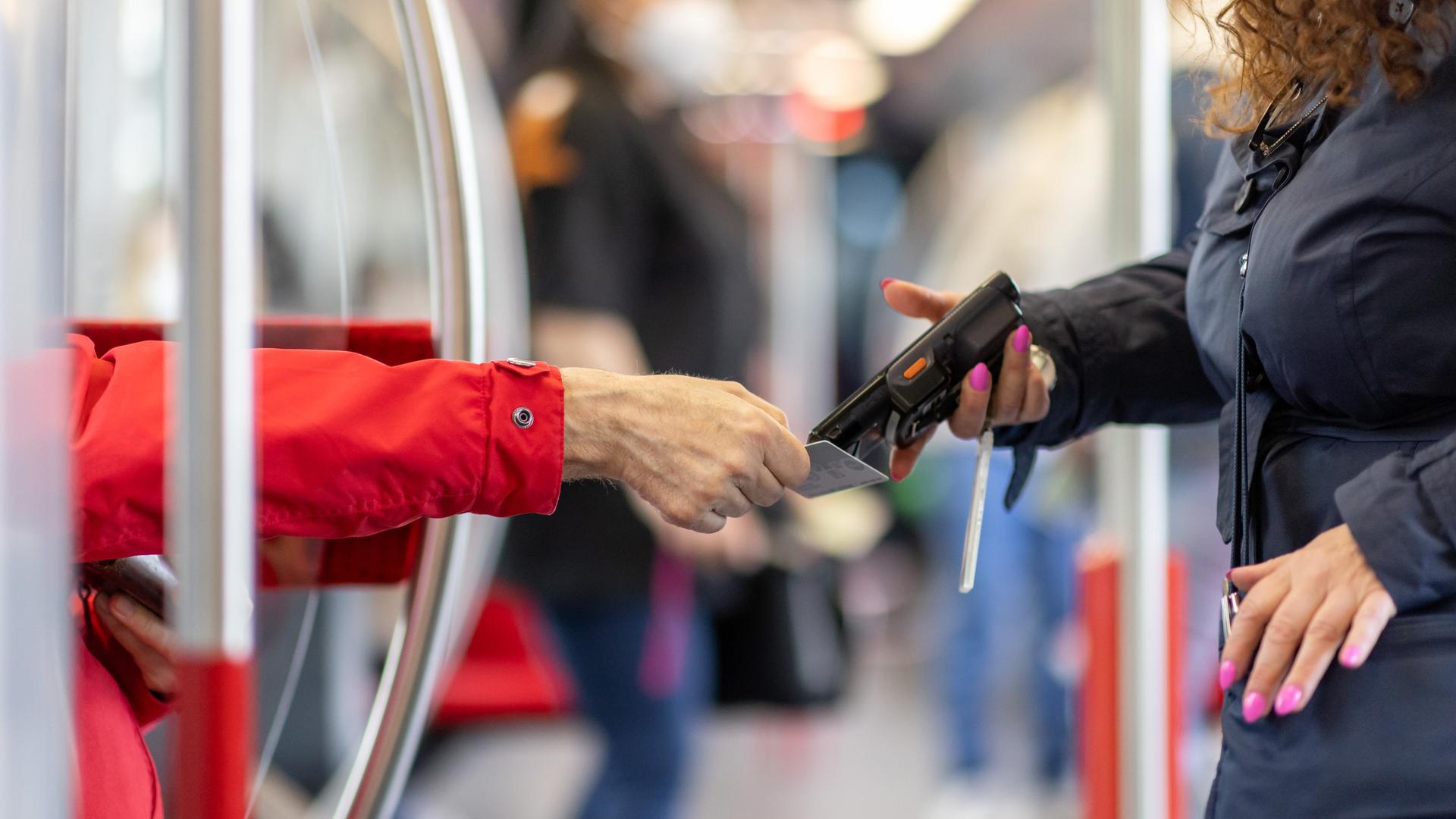 Eine Fahrkartenkontrolleurin kontrolliert mit einem elektronischen Lesegerät den Fahrschein von einem Fahrgast. Eine Fahrkartenkontrolleurin kontrolliert mit einem elektronischen Lesegerät den Fahrschein von einem Fahrgast.