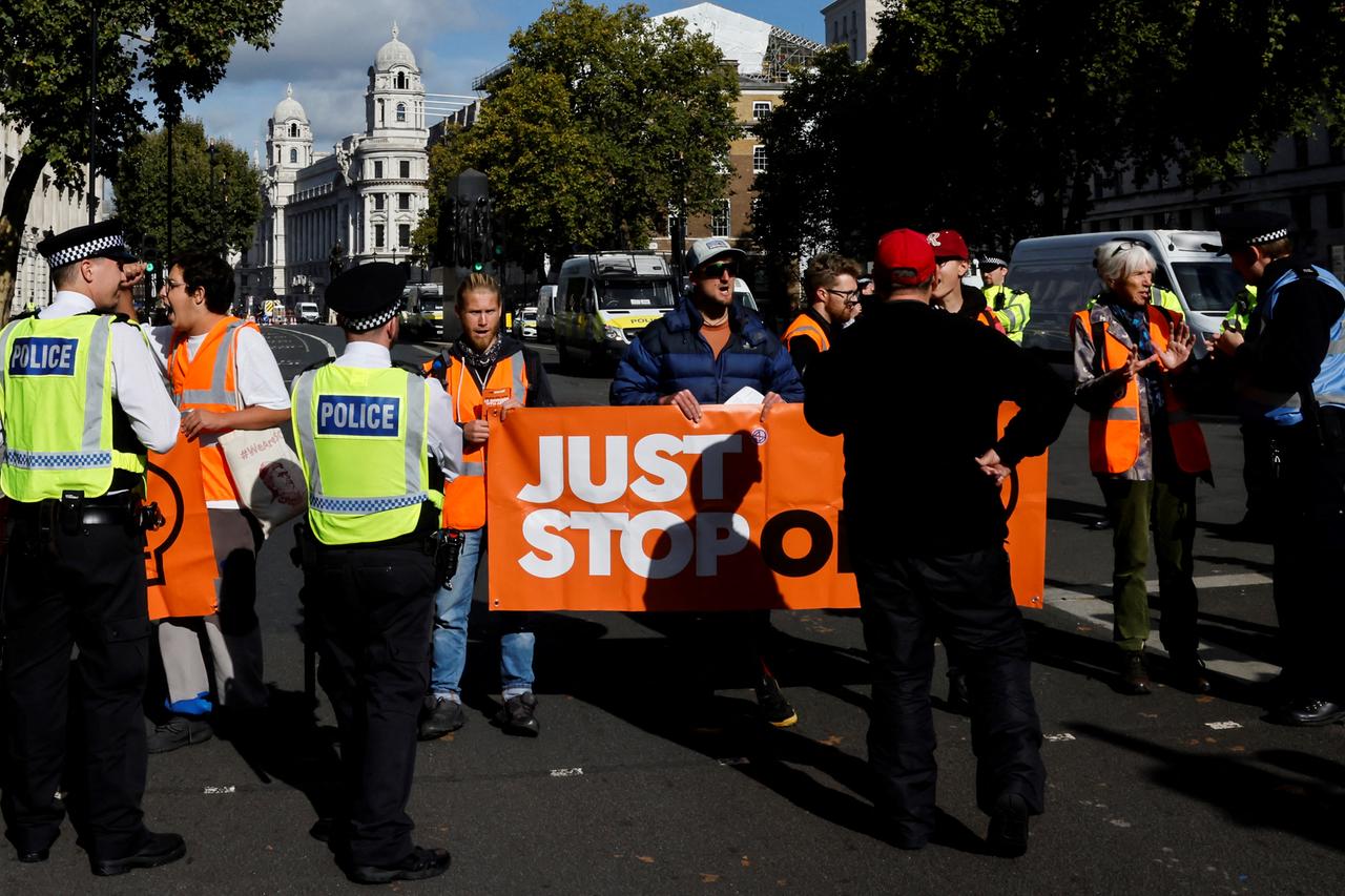 組織のメンバー "油を止めるだけ" ロンドンのダウニング街にある英国首相官邸の外での抗議。 彼らは NGO の名前が書かれた横断幕を掲げ、警官が前に立っています。