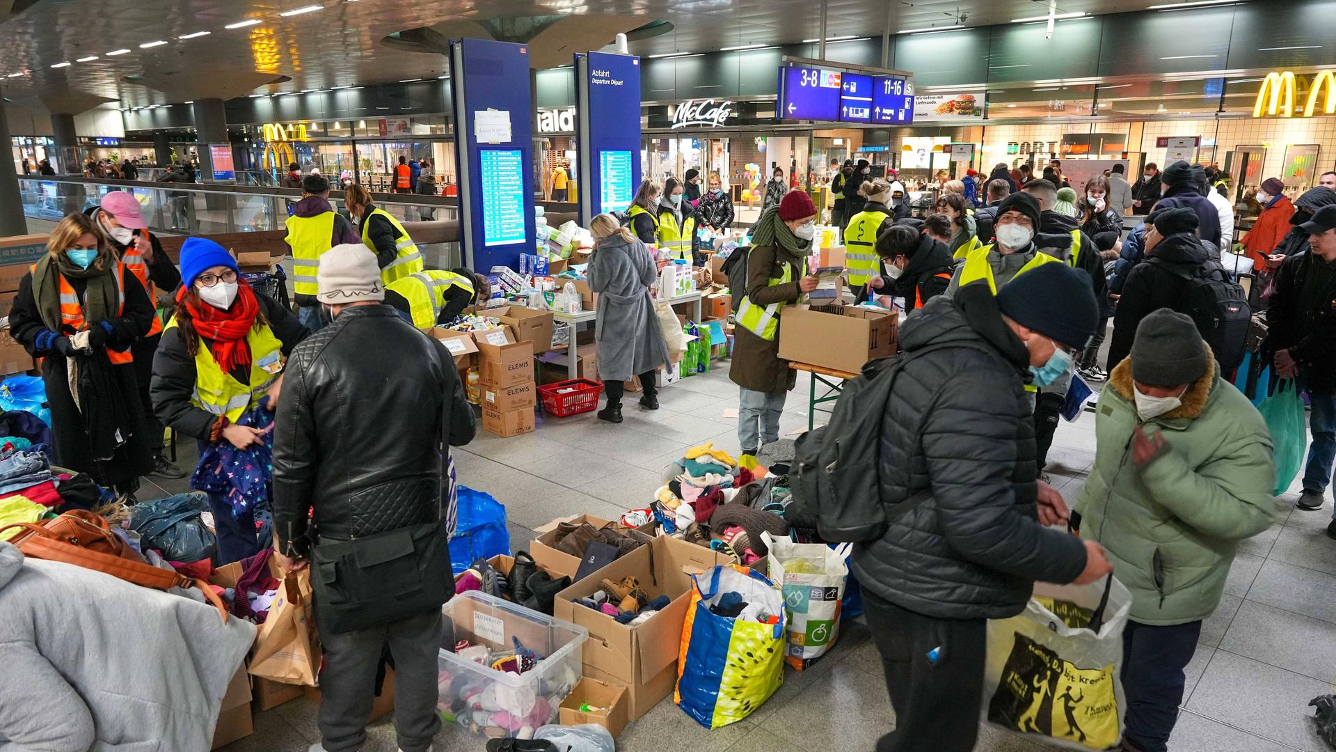 Maskierte Menschen am Bahnhof mit Kisten voller Kleidung.