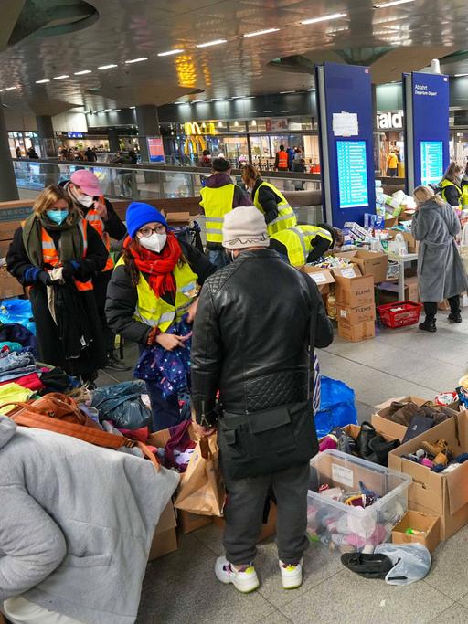 Maskierte Menschen am Bahnhof mit Kisten voller Kleidung.