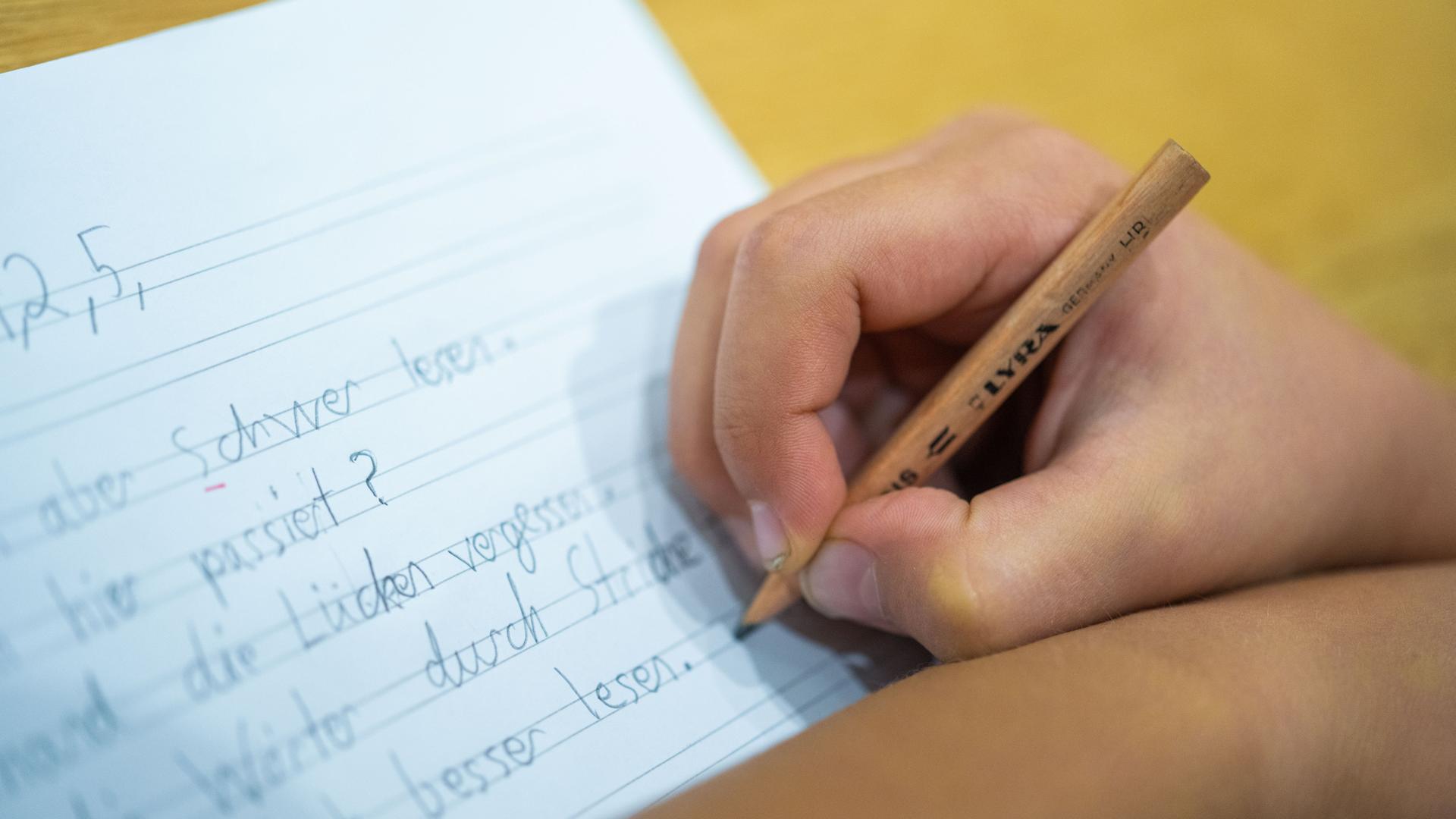 Grundschüler schreibt mit einem Bleistift auf ein Blatt.