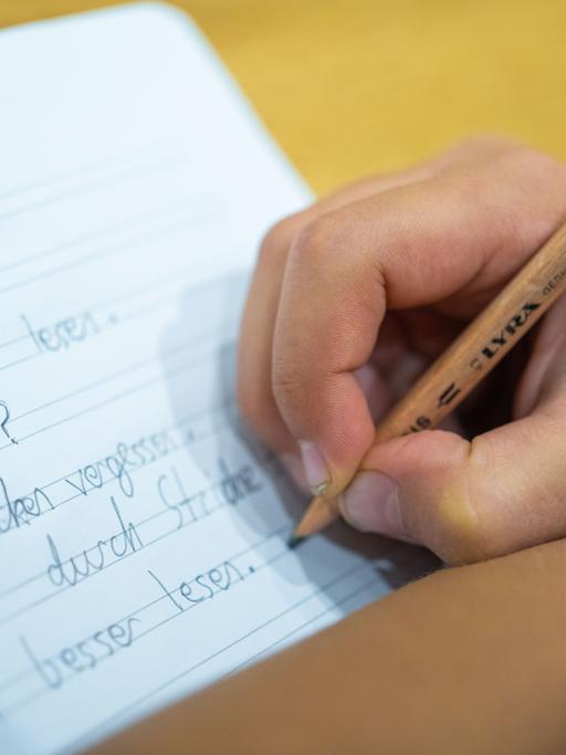 Grundschüler schreibt mit einem Bleistift auf ein Blatt.