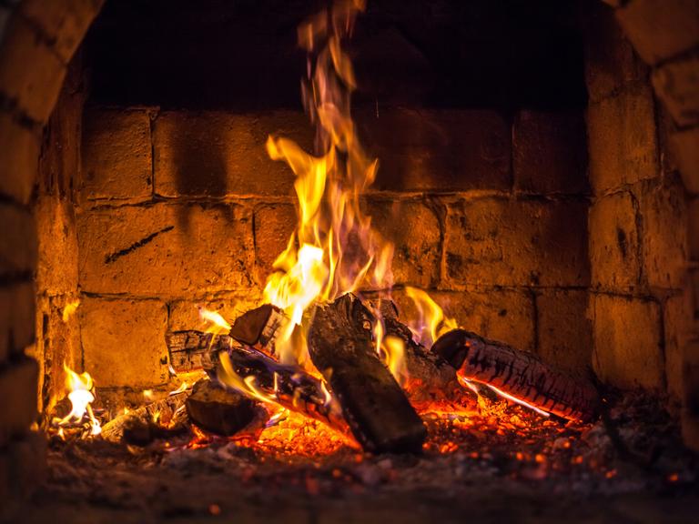 Ein Feuer brennt in einem Kamin. Er ist aus großen Steinen gebaut.
