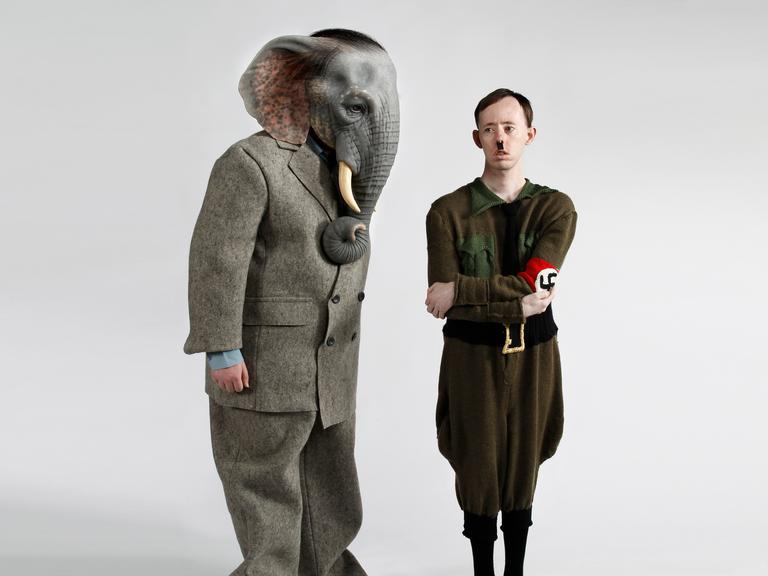 Ein Schauspieler mit einer Elefantenkopfmaske und ein zweiter, der Hitler darstellt, stehen auf einer Bühne.
