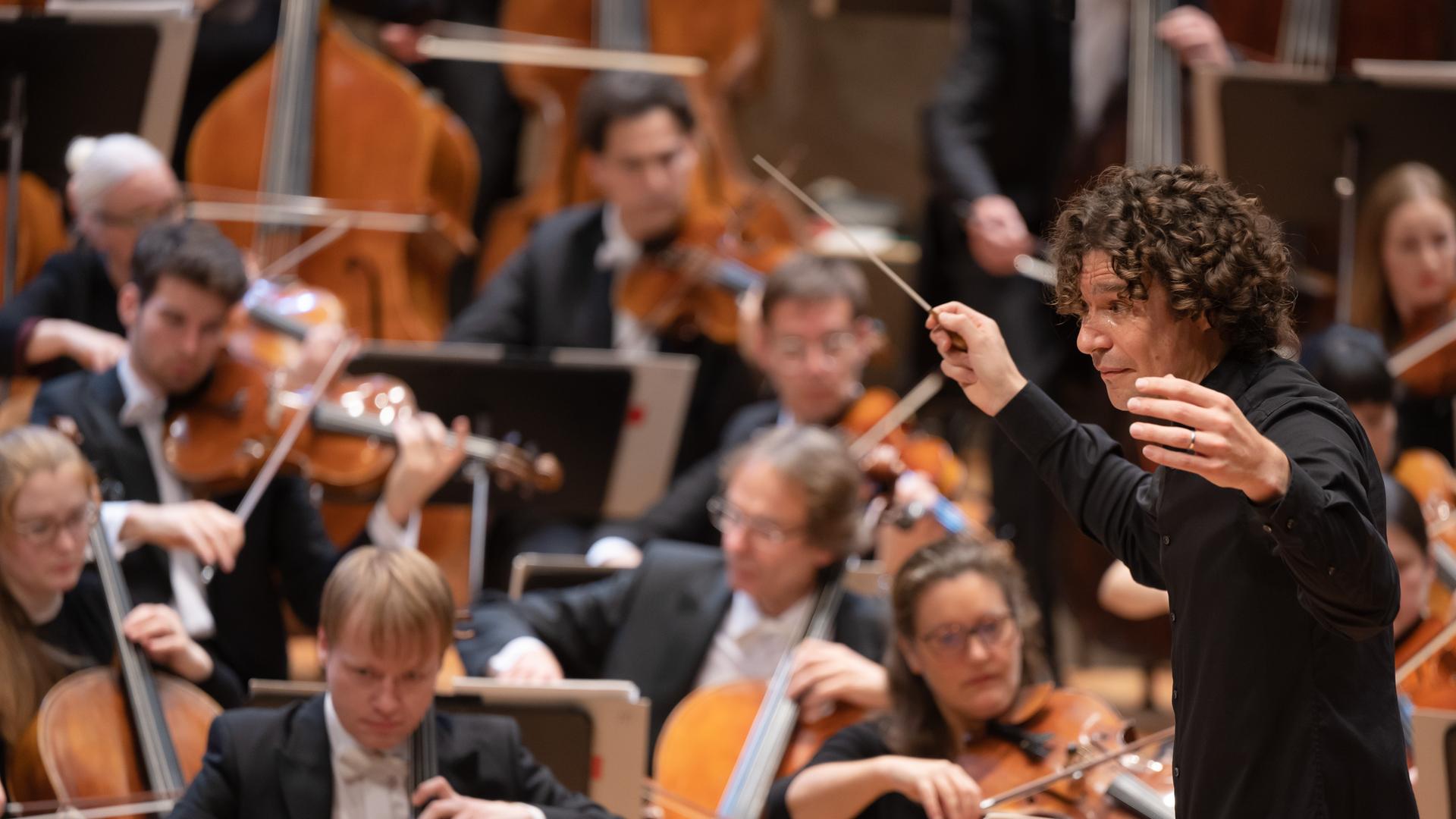 Dirigent Robin Ticciati öffnet seine Arme weit Richtung Orchester. Dirigent Robin Ticciati öffnet seine Arme weit Richtung Orchester.