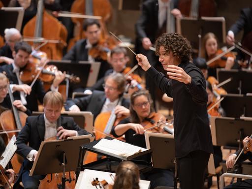 Dirigent Robin Ticciati öffnet seine Arme weit Richtung Orchester.