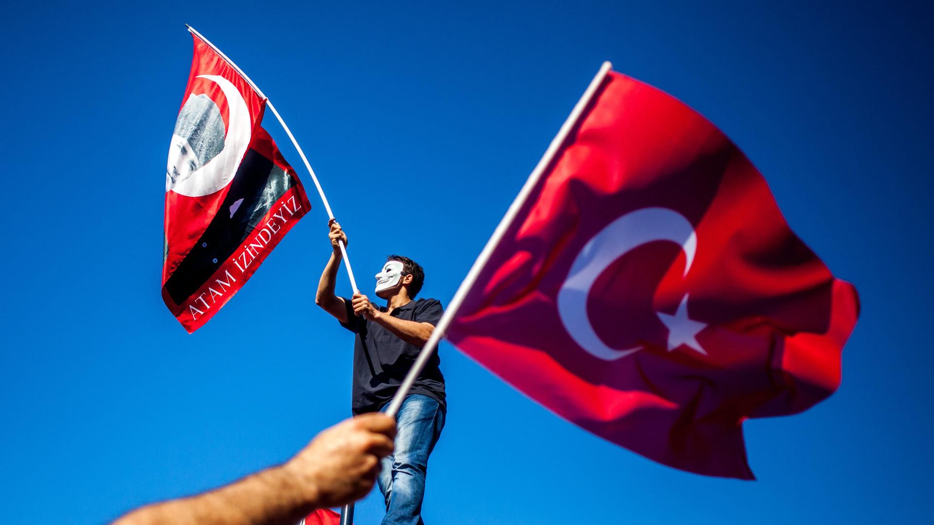 Ein Demonstrant mit Anonymous-Maske und Atatürk-Fahne, davor eine Türkei-Fahne. 