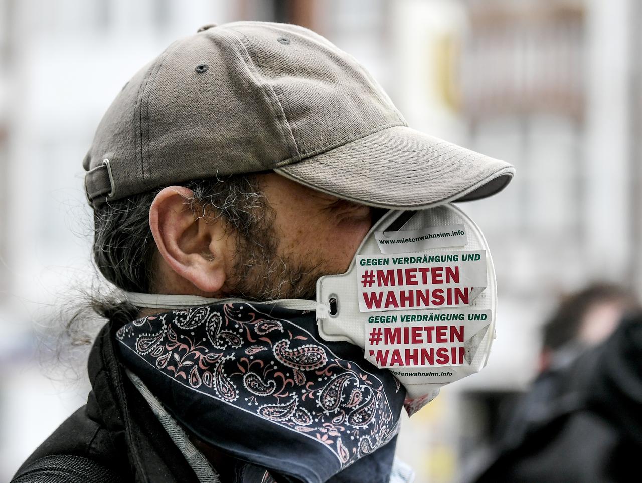 Ein Demonstrant trägt einen Mundschutz an dem ein Aufkleber mit der Aufschrift «Gegen Verdrängung und Mieten Wahnsinn» geklebt ist.