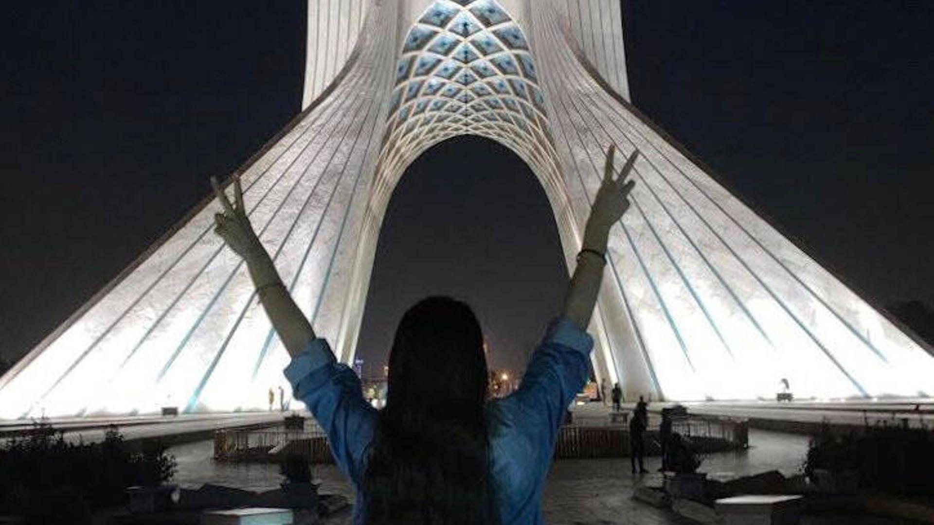Eine Frau ist anonym von hinten ohne Kopftuch vor einem Gebäude in Teheran zu sehen.
