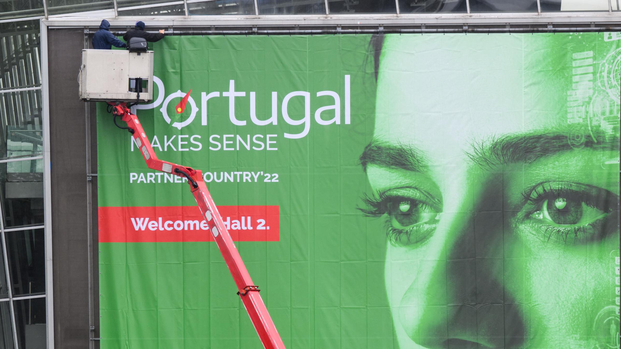 Zwei Arbeiter installieren bei den Aufbauarbeiten für die Hannover Messe 2022 ein Werbebanner vom Partnerland Portugal. Die weltgröÃte Industriemesse Hannover Messe findet vom 30. Mai bis 2. Juni statt.
