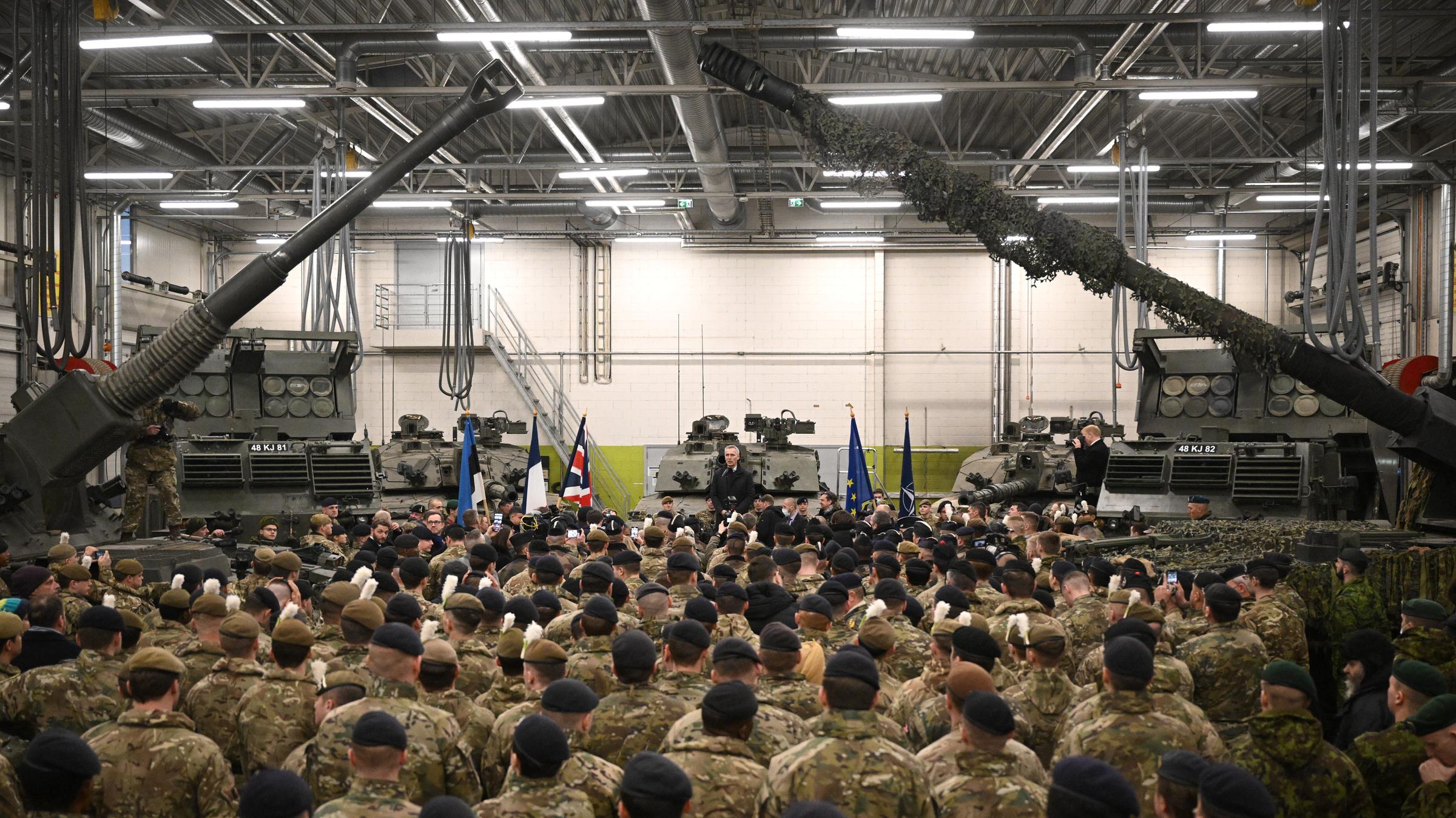 Jens Stoltenberg spricht vor Nato-Truppen in der Tapa Militärbasis. Die Zielfernrohre zweier Panzer rahmen das Bild.