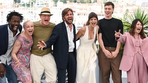Männer und Frauen des Filmteams bewegen sich fröhlich schreiend in einer Reihe auf die Kameras in Cannes zu.