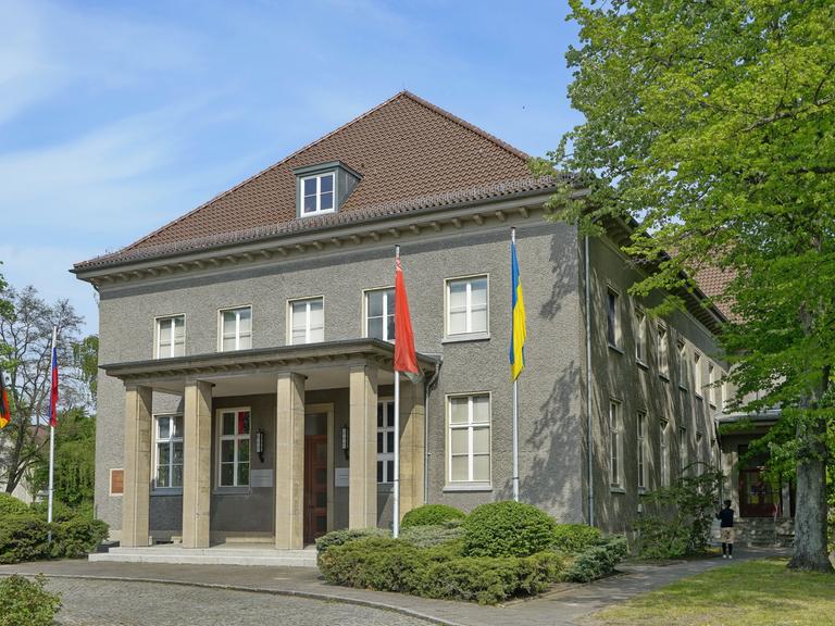 Blick auf das Deutsch-Russische Museum in Berlin-Karlshorst, vor dem die deutsche, die russische, die ukrainische und die belarussiche Flagge zu sehen sind.